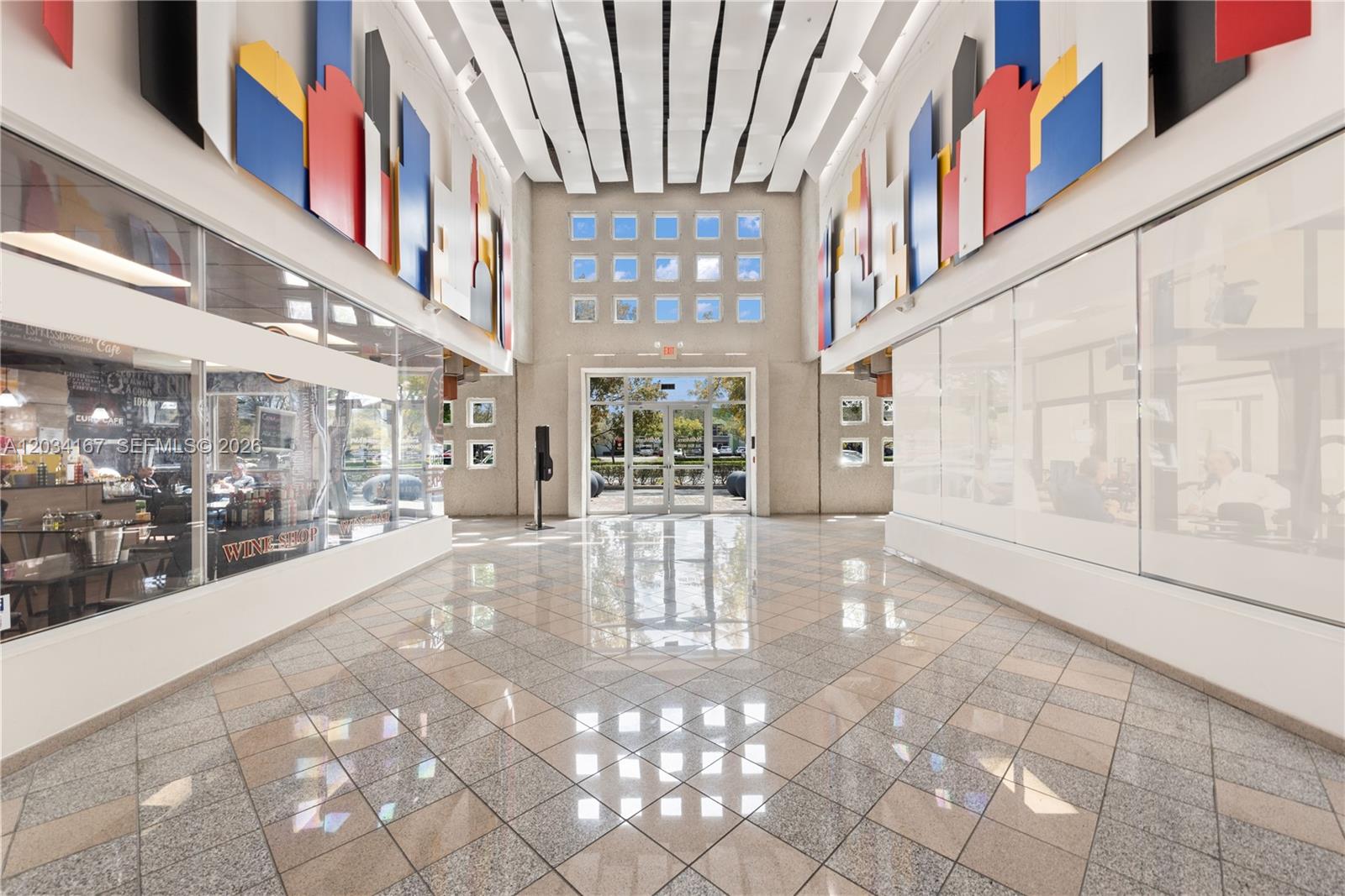 A bright, tiled lobby features glass-walled storefronts, colorful wall art, and a central glass entrance — DORAL, FL
