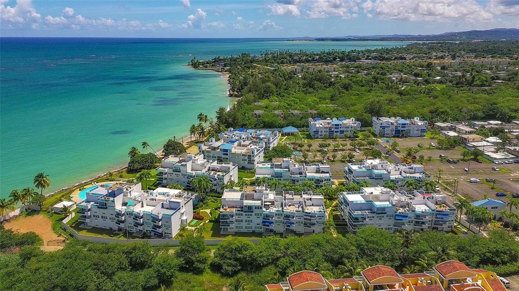 An aerial view shows a coastal apartment complex with white buildings near a turquoise beach — 187 km 7 BO. MEDIANIA ALTA UNIT 401, LOIZA, PR