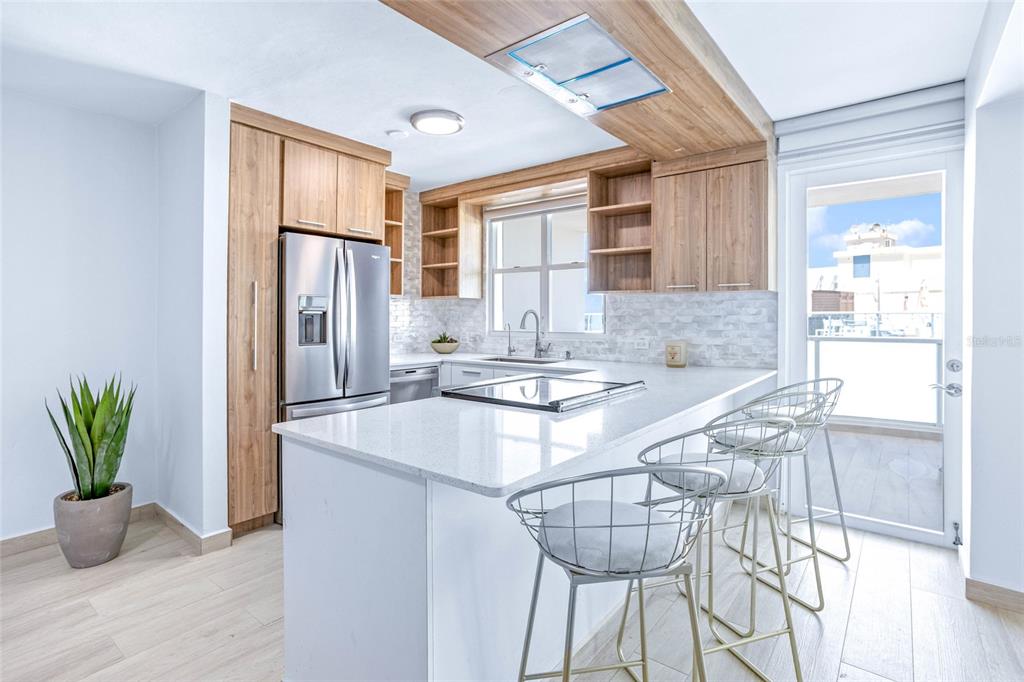 A modern kitchen features light wood cabinetry, white countertops, a breakfast bar, and a balcony door — 187 km 7 BO. MEDIANIA ALTA UNIT 401, LOIZA, PR
