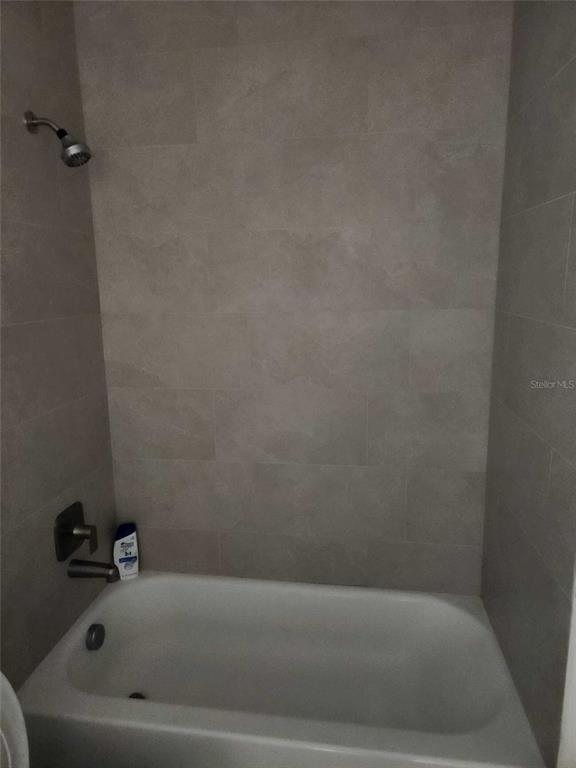 A bathtub with a shower head and neutral-toned wall tiles in a bathroom — 7369 SEALAWN DRIVE, SPRING HILL, FL