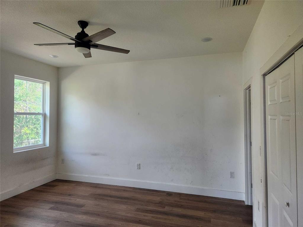 An empty bedroom features wood-look flooring, white walls, a ceiling fan, and a closet door — 7369 SEALAWN DRIVE, SPRING HILL, FL