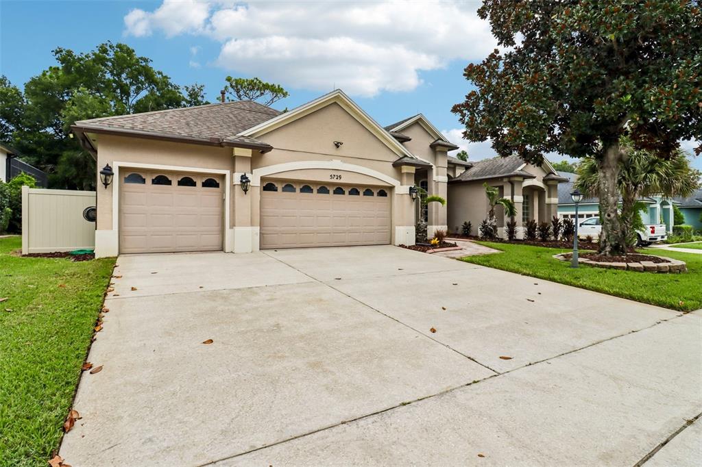 A beige single-story house features a three-car garage and a concrete driveway — 5729 OAK LAKE TRAIL, OVIEDO, FL