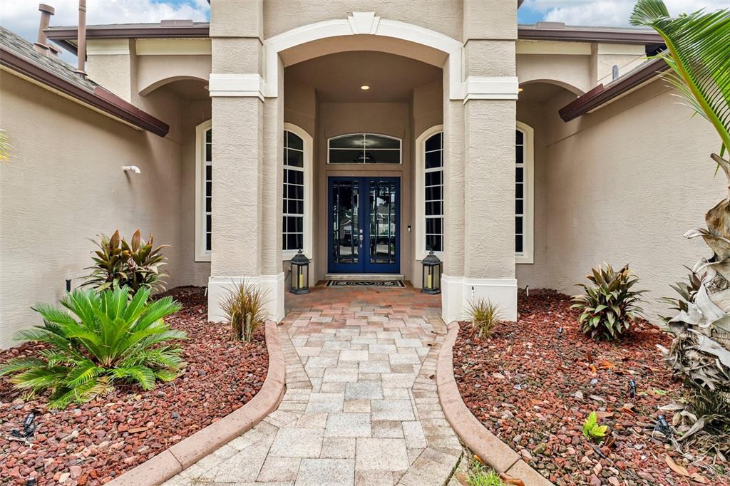 The exterior entrance features a paved walkway leading to double blue doors under an archway — 5729 OAK LAKE TRAIL, OVIEDO, FL