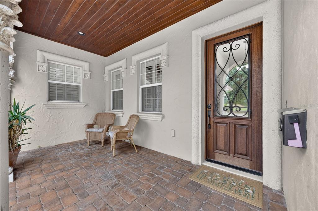 A covered front porch with brick flooring, two wicker chairs, and a wooden front door — 341 E READING WAY, WINTER PARK, FL