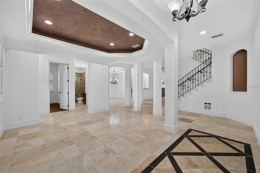 A spacious foyer features light tile flooring, a dark tray ceiling, and a wrought-iron staircase — 341 E READING WAY, WINTER PARK, FL