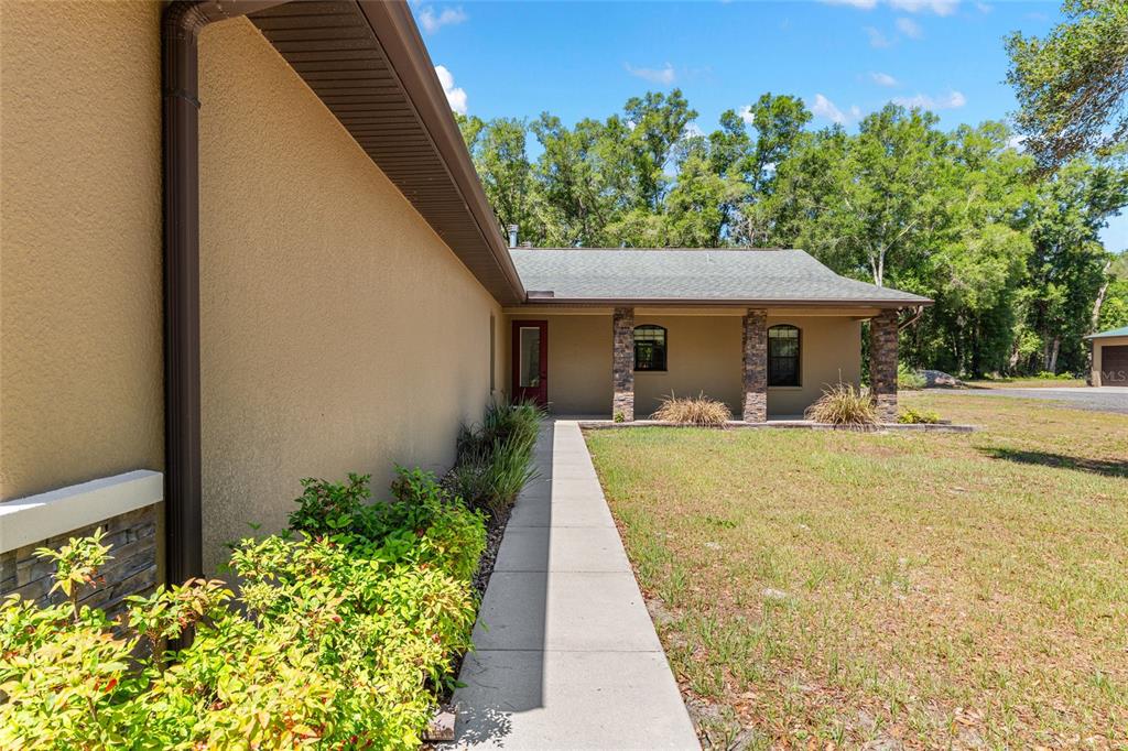 A concrete walkway leads to the covered front entrance of a tan house with stone pillars — 5190 NW 90TH AVENUE, CHIEFLAND, FL