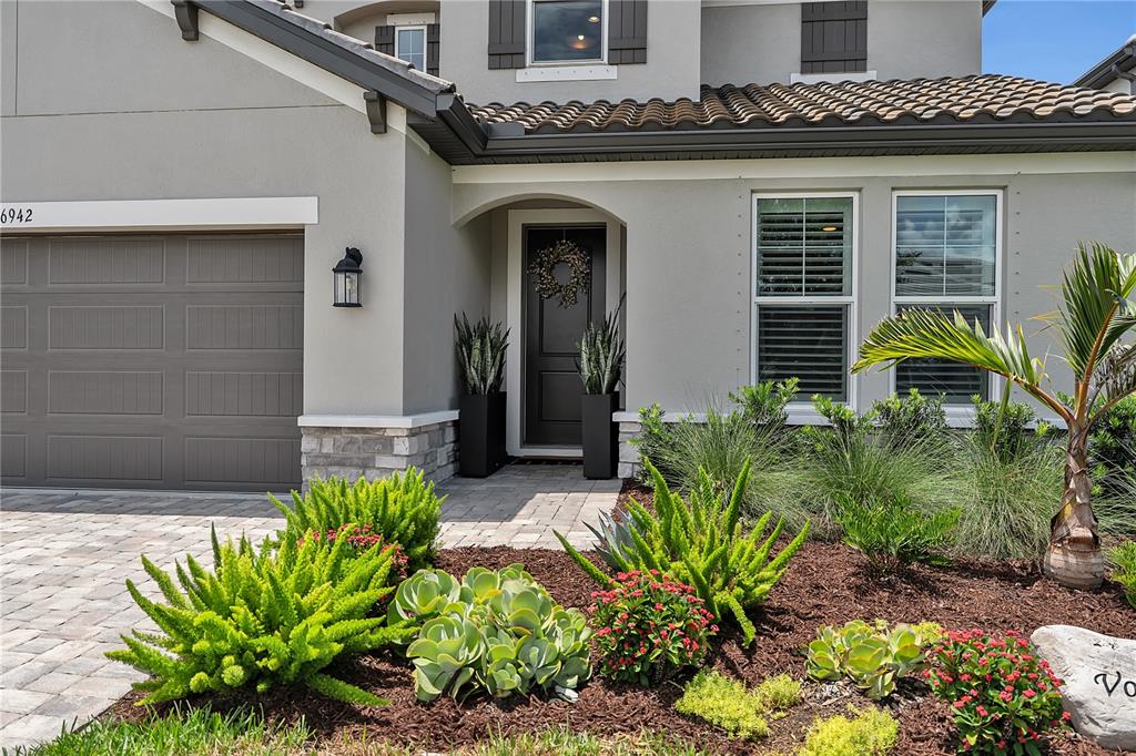 The exterior of a house features a gray garage, a front door, and landscaped garden beds — 16942 SAVORY MIST CIRCLE, BRADENTON, FL