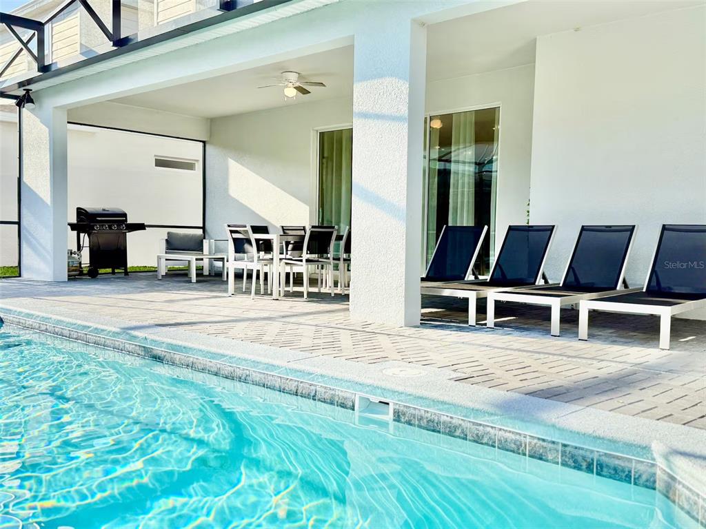 A covered patio features a swimming pool, dining set, grill, and several lounge chairs — 4453 KAIPO ROAD, DAVENPORT, FL