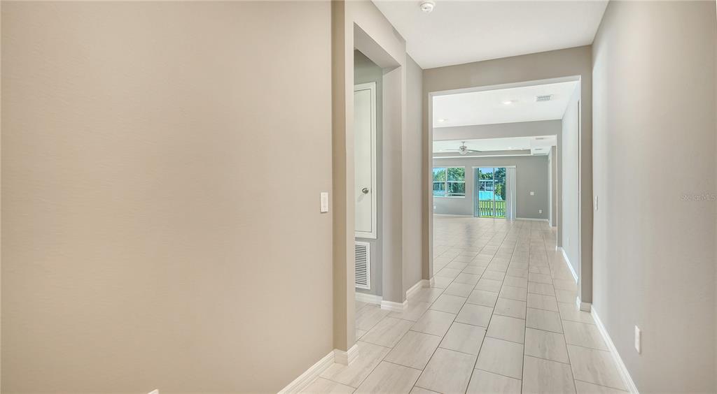 A hallway with light tile flooring leads toward an open living area with large windows — 14239 59TH CIRCLE E, BRADENTON, FL
