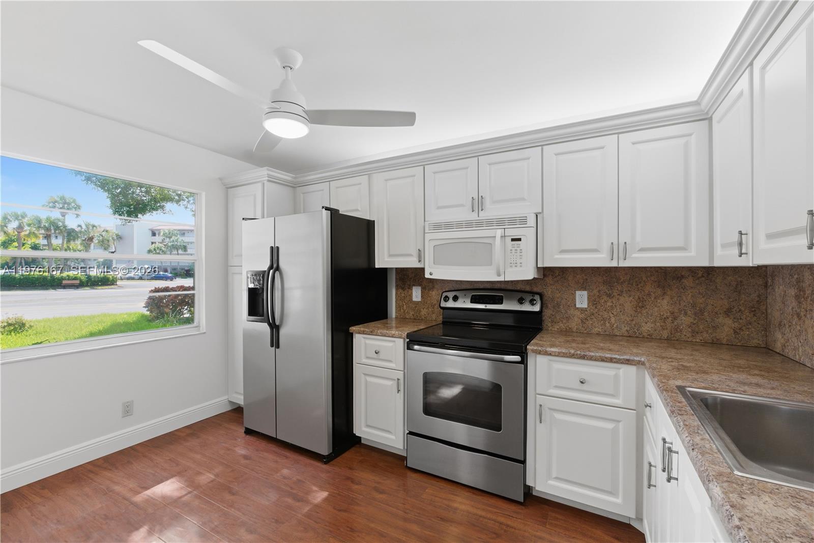 A kitchen features white cabinets, stainless steel appliances, a brown countertop, and wood-look flooring — 1901 Bermuda Cir # A1, Coconut Creek FL 33066, COCONUT CREEK, FL