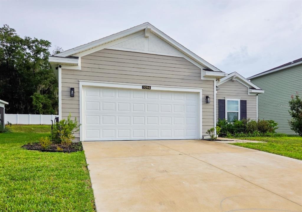 A tan, single-story house with a white two-car garage and a concrete driveway — 3294 NE 38TH LANE, OCALA, FL