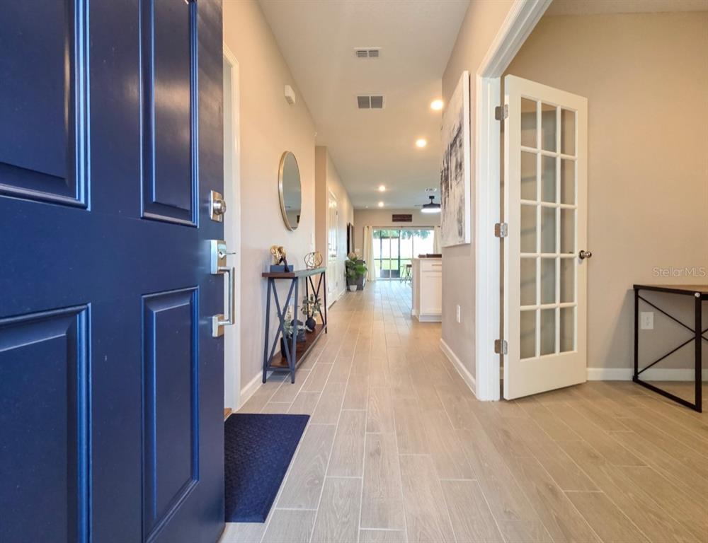A view from a blue front door down a hallway with light wood-look tile flooring — 3294 NE 38TH LANE, OCALA, FL