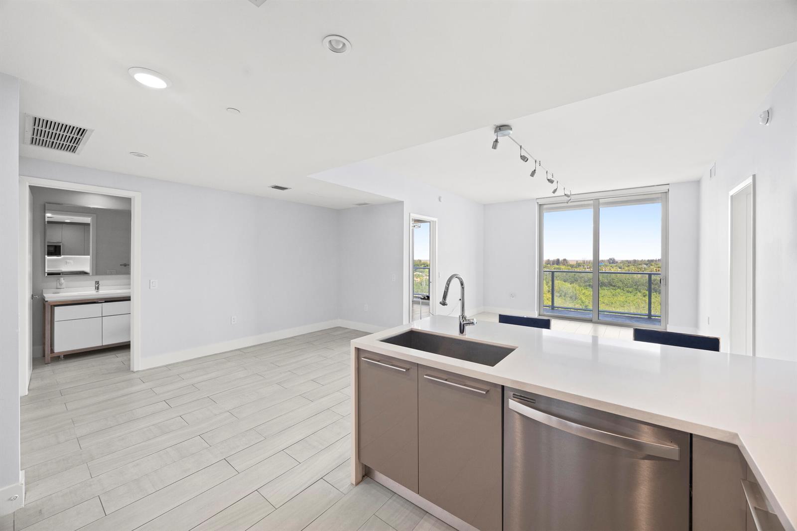 A modern kitchen island with a stainless steel sink overlooks an open living area — 2000 Metropica Way # 802, Sunrise FL 33323, SUNRISE, FL