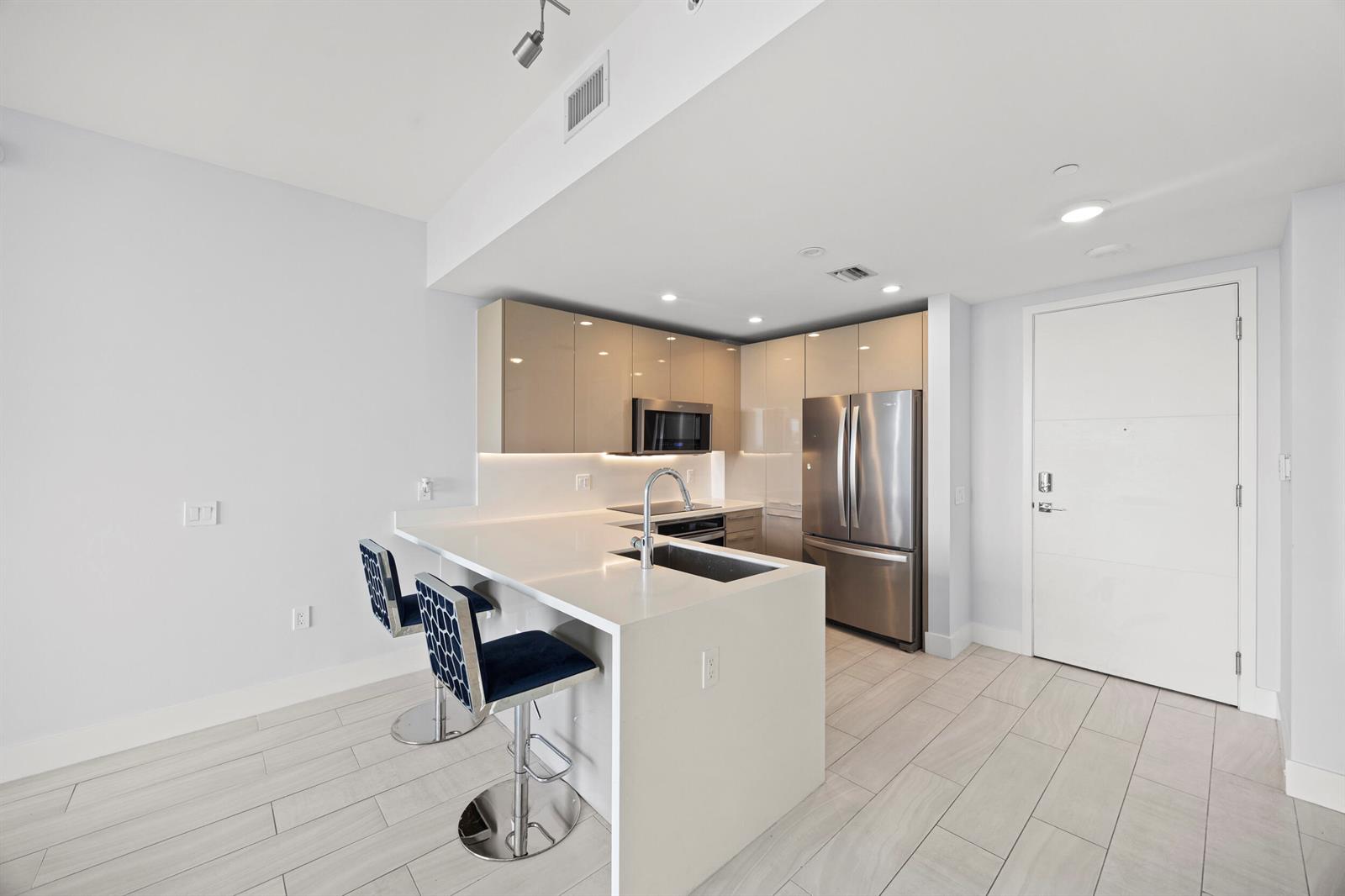 A modern kitchen features a white quartz island, stainless steel appliances, and light-colored cabinetry — 2000 Metropica Way # 802, Sunrise FL 33323, SUNRISE, FL
