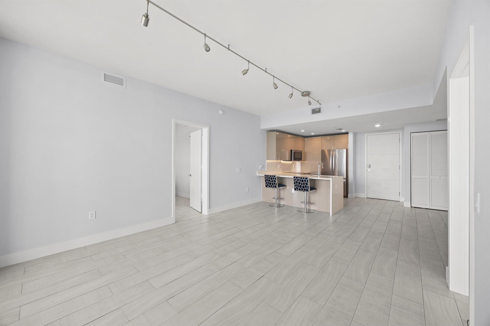 An open-concept living area features light gray tile flooring, a track lighting system, and a kitchen — 2000 Metropica Way # 802, Sunrise FL 33323, SUNRISE, FL