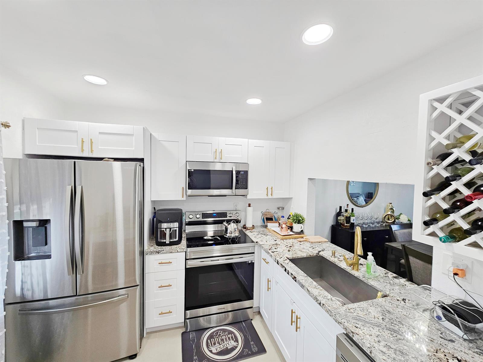 A kitchen features white cabinets, stainless steel appliances, granite countertops, and a wine rack — 7807 Golf Cir Circle # 305, Margate FL 33063, MARGATE, FL