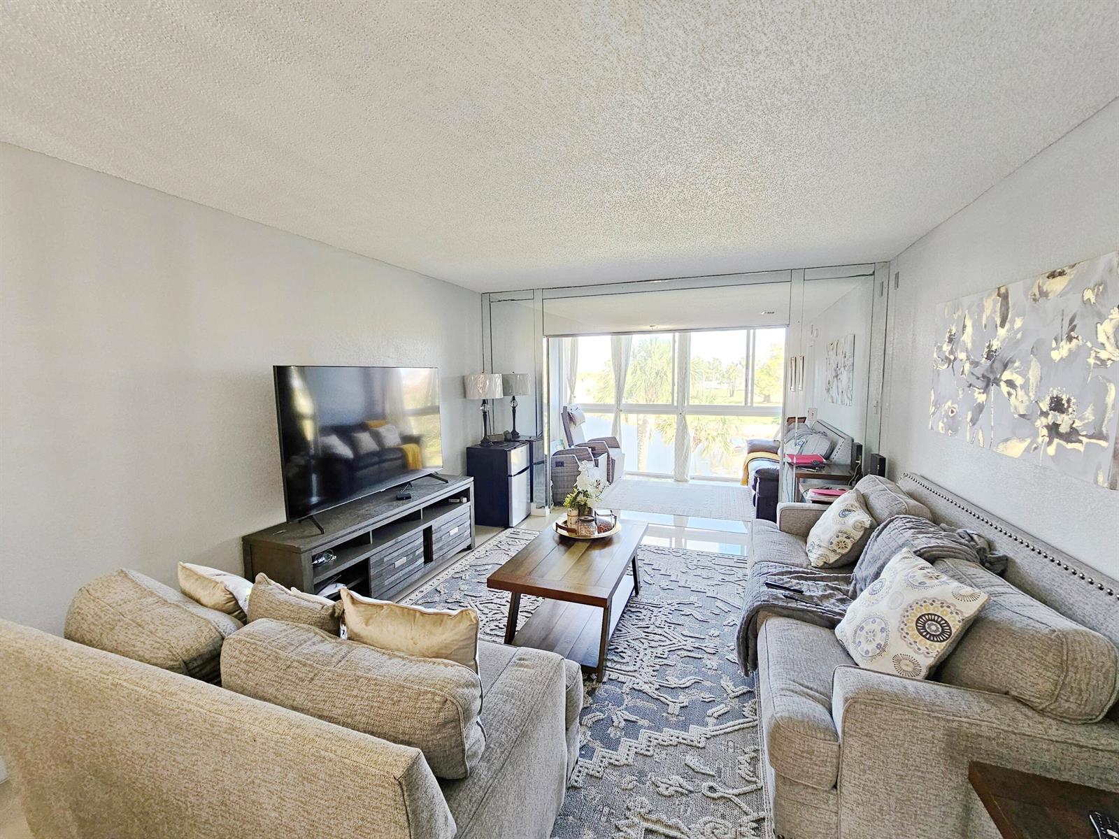 A living room features a grey sofa, a coffee table, and a television on a stand — 7807 Golf Cir Circle # 305, Margate FL 33063, MARGATE, FL