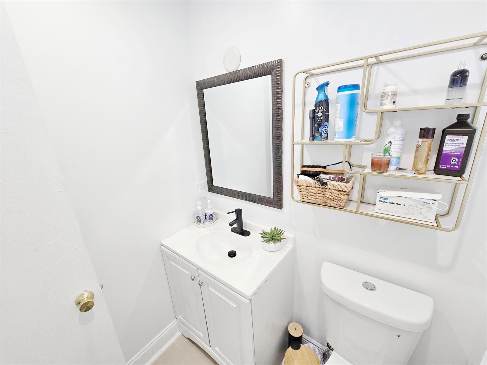 A small bathroom features a white vanity, a dark-framed mirror, and gold wall shelving — 7807 Golf Cir Circle # 305, Margate FL 33063, MARGATE, FL
