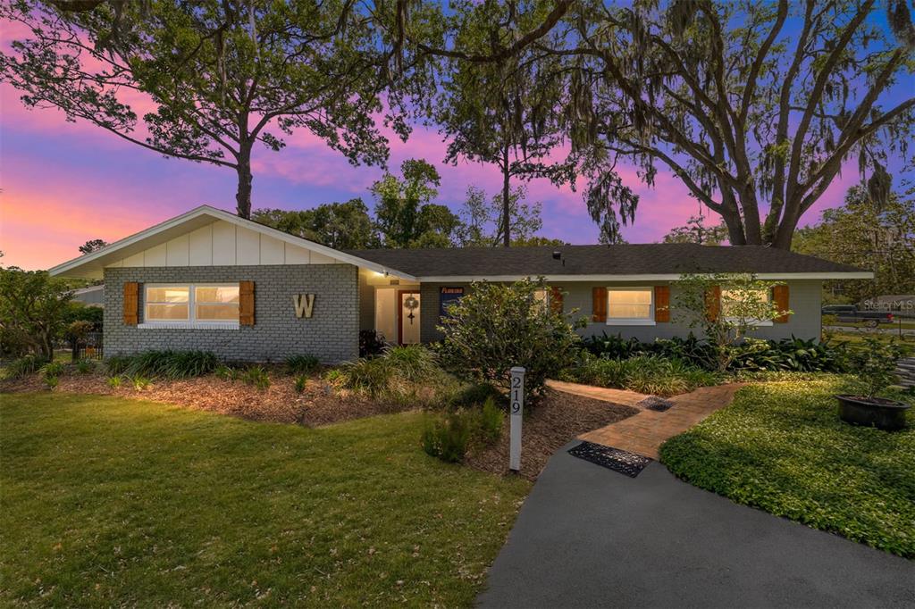 A single-story gray brick house with a paved walkway and large trees at sunset — 219 SE 20TH TERRACE, OCALA, FL