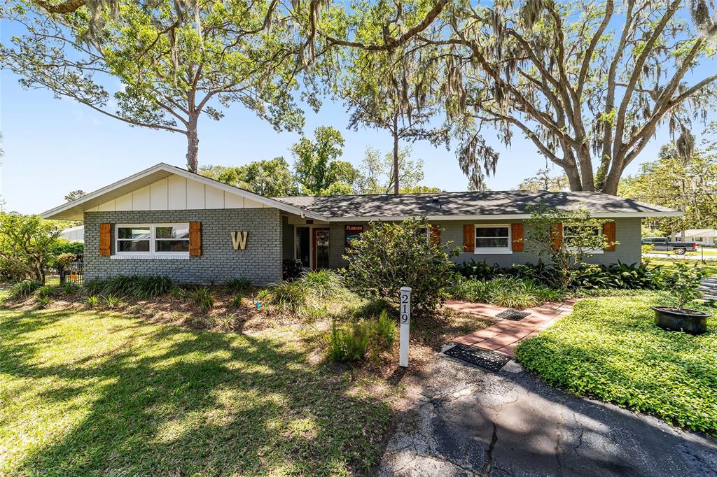 A single-story gray brick house with a white gable and large trees in the yard — 219 SE 20TH TERRACE, OCALA, FL