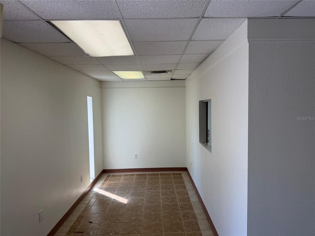 An empty room features beige tile flooring, white walls, and a drop ceiling with lights — 3434 SW 24TH AVENUE UNIT D, GAINESVILLE, FL
