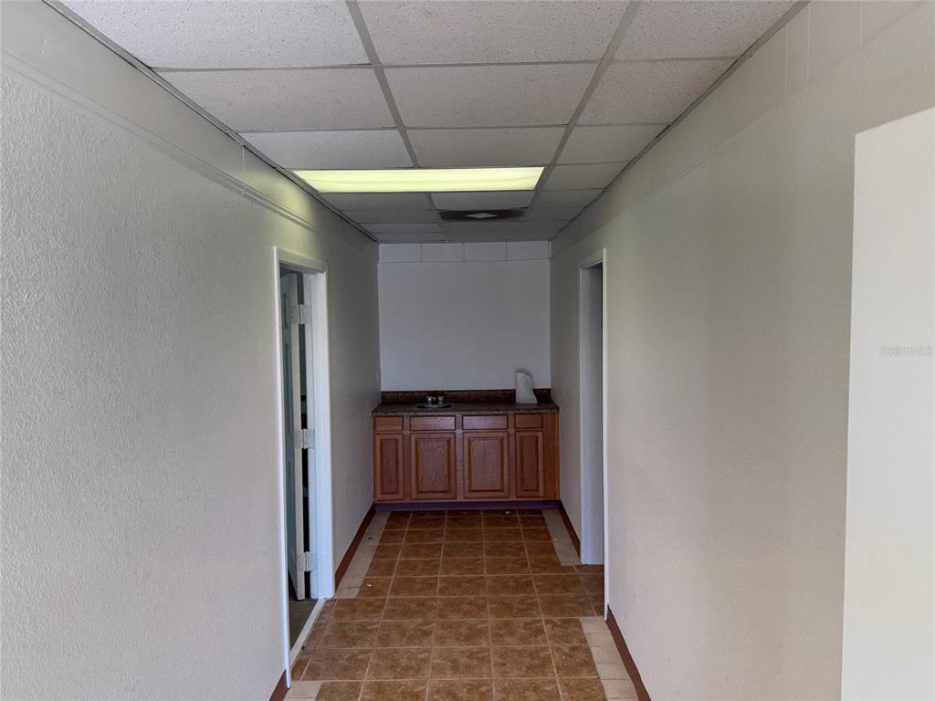 A narrow hallway features a drop ceiling, tile flooring, and a small kitchenette at the end — 3434 SW 24TH AVENUE UNIT D, GAINESVILLE, FL