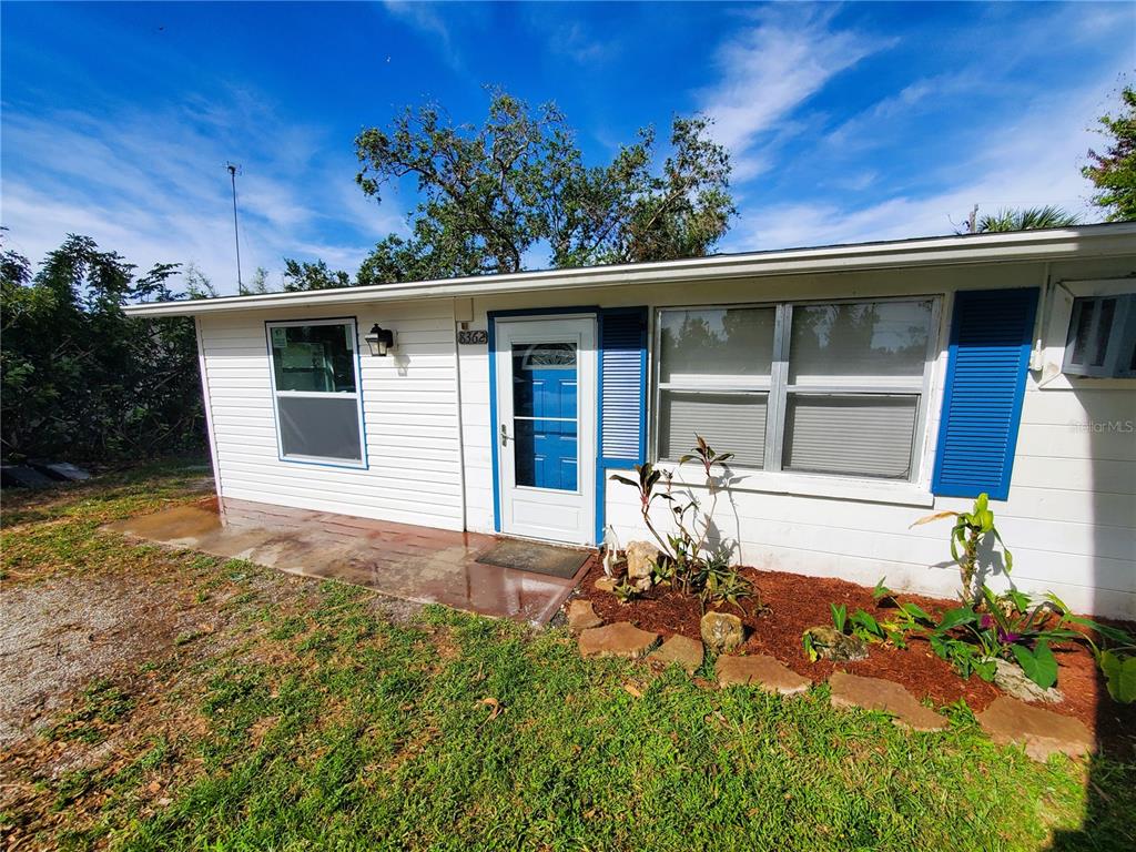 A white single-story house exterior features a blue front door, shutters, and a small garden — 8362 OSPREY ROAD, ENGLEWOOD, FL