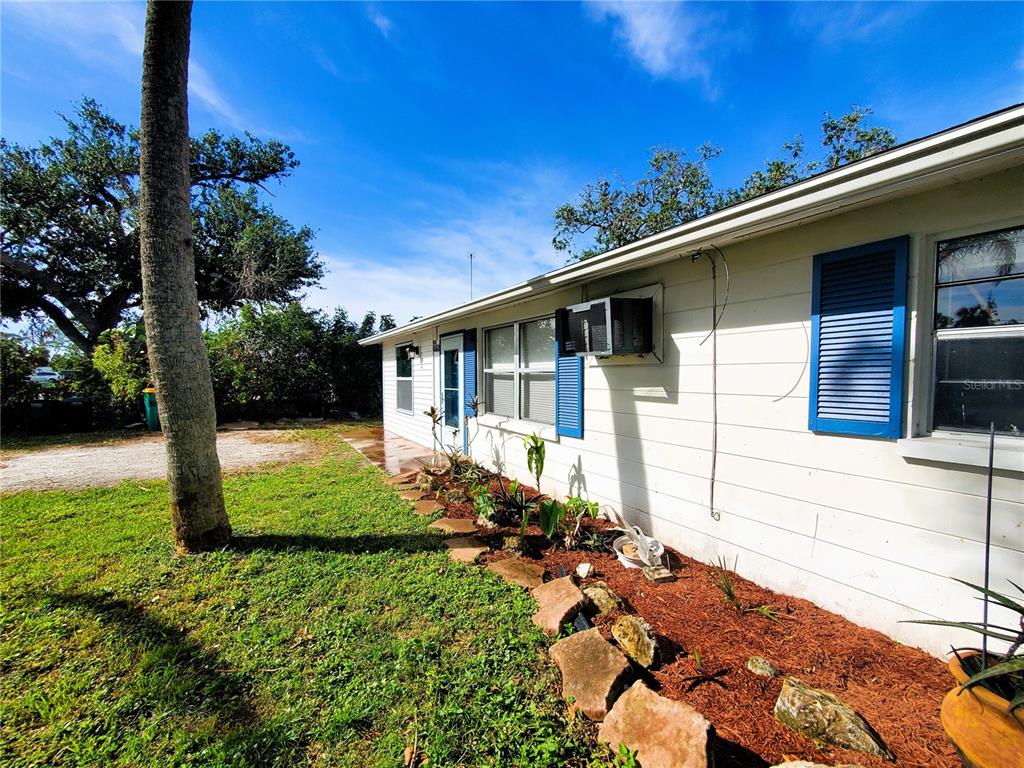 A single-story house exterior with white siding, blue shutters, and a landscaped garden bed — 8362 OSPREY ROAD, ENGLEWOOD, FL