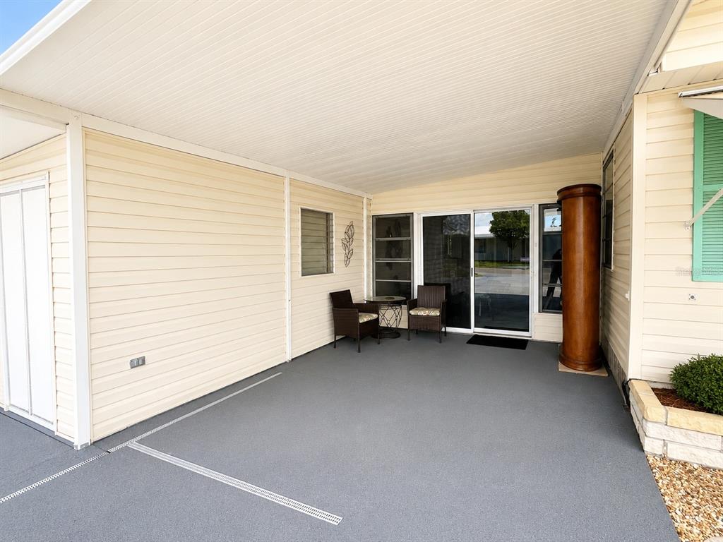A covered patio features light-colored siding, a gray floor, and two chairs near sliding doors — 1912 INDIANA AVENUE, BRADENTON, FL