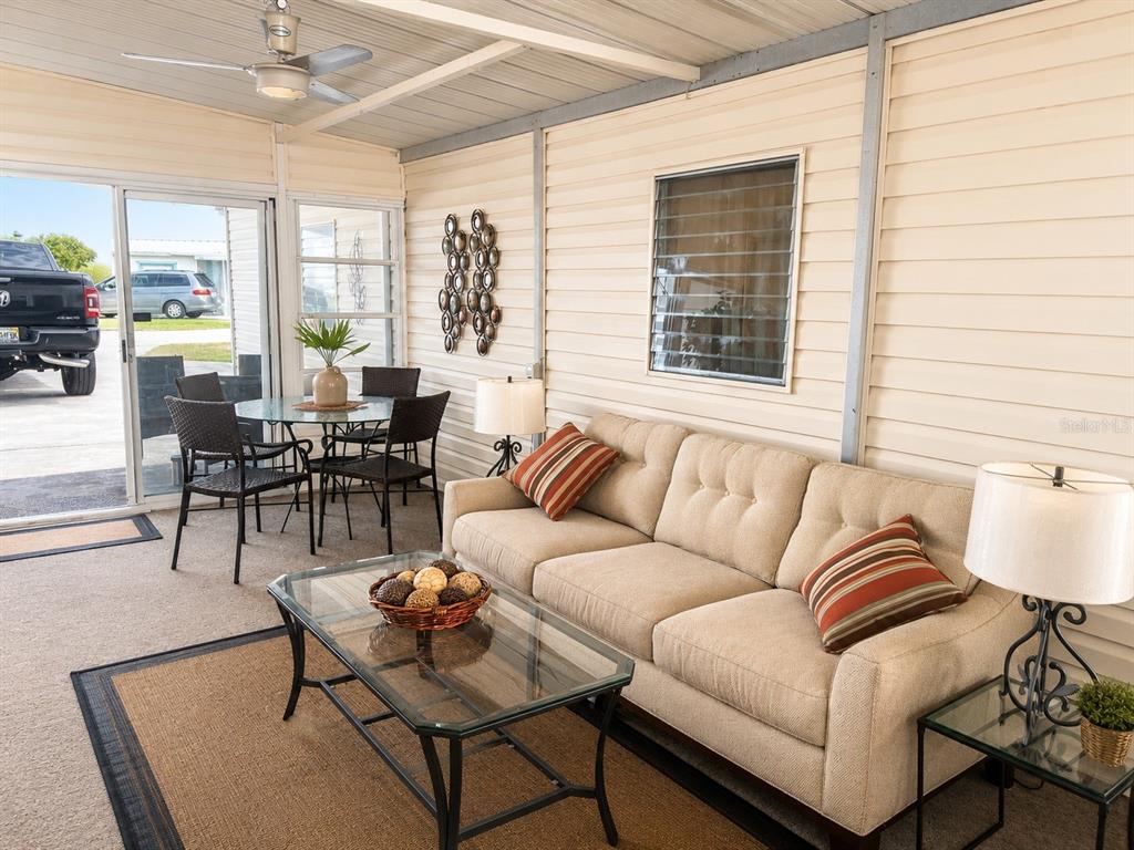 A sunroom features a beige sofa, glass coffee table, dining set, and a ceiling fan — 1912 INDIANA AVENUE, BRADENTON, FL