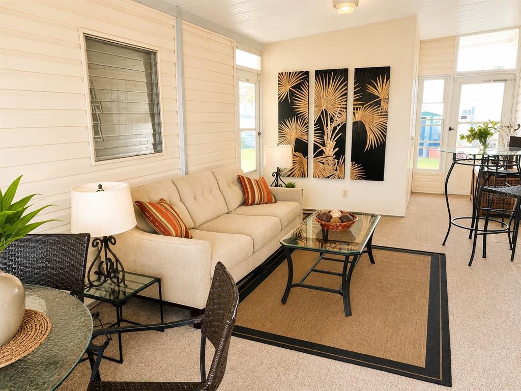 A sunroom features a beige sofa, glass coffee table, and black-framed wall art — 1912 INDIANA AVENUE, BRADENTON, FL