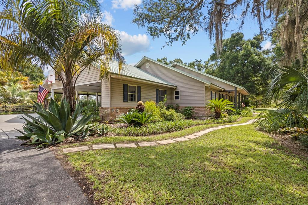 A tan house with a metal roof, carport, and a stone walkway through the lawn — 8851 NW 115TH STREET, CHIEFLAND, FL