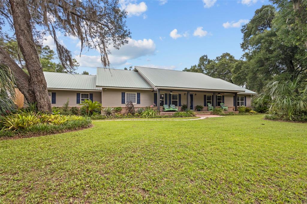 A single-story house with a metal roof and a covered porch sits on a lawn — 8851 NW 115TH STREET, CHIEFLAND, FL