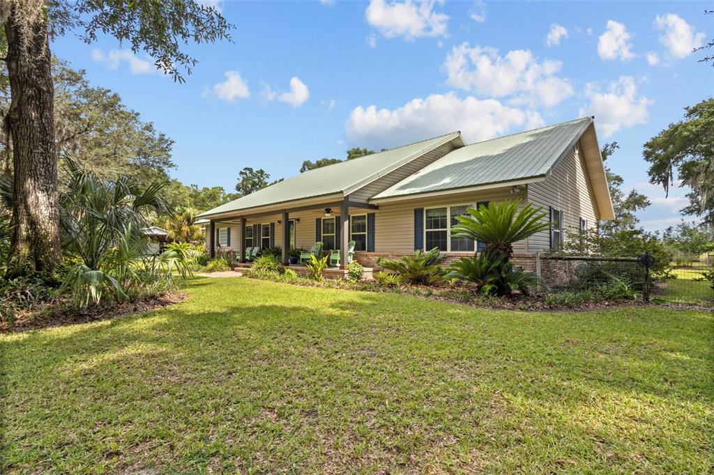 A single-story house with tan siding, a green metal roof, and a covered front porch — 8851 NW 115TH STREET, CHIEFLAND, FL