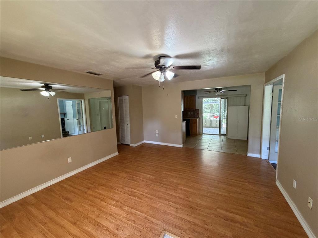 A living room with wood-look flooring, a ceiling fan, and a large wall mirror — 4557 SE 140TH PLACE, SUMMERFIELD, FL