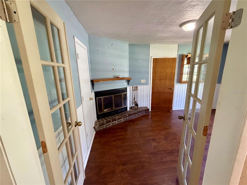 A room with wood-look flooring, a brick fireplace, and white wainscoting viewed through French doors — 4557 SE 140TH PLACE, SUMMERFIELD, FL