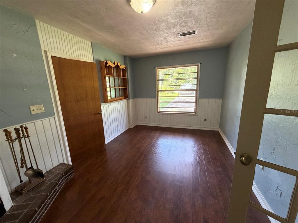 A room with wood-look flooring, white wainscoting, a window, and a fireplace tool set — 4557 SE 140TH PLACE, SUMMERFIELD, FL