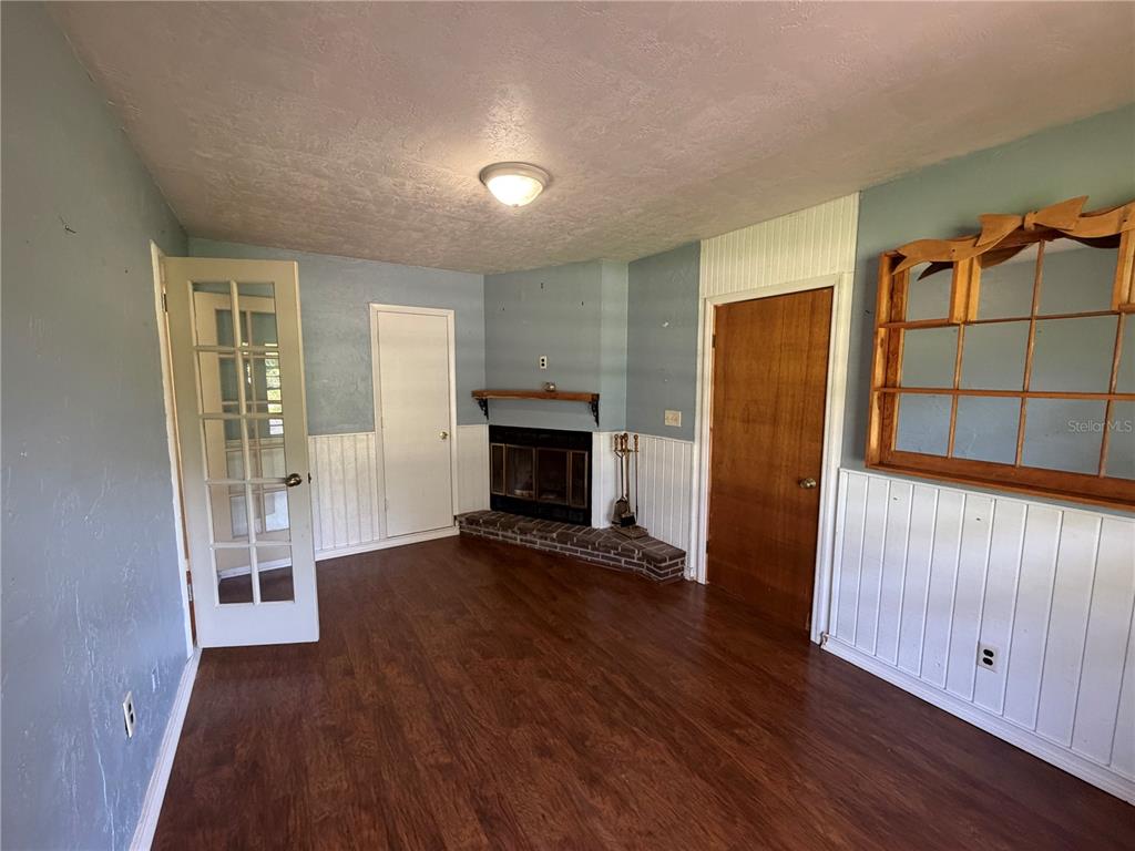 A room with wood-look flooring, a brick fireplace, white wainscoting, and a wooden wall shelf — 4557 SE 140TH PLACE, SUMMERFIELD, FL