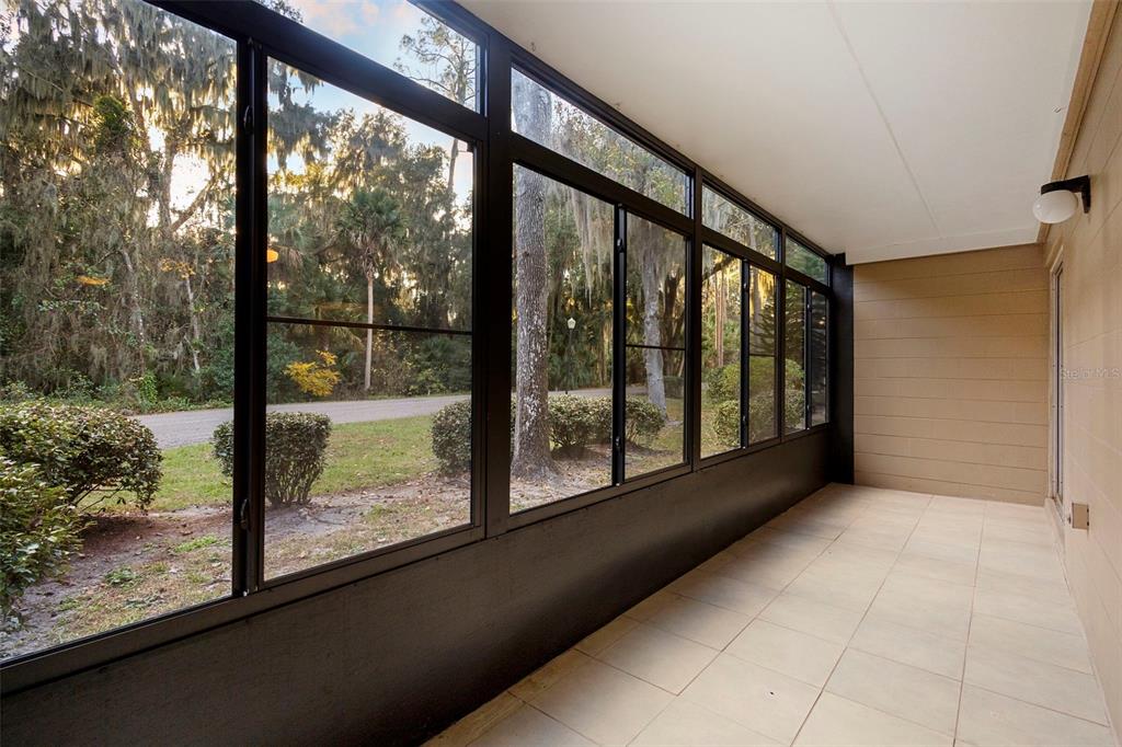 A sunroom with large windows, tiled flooring, and a view of trees and a road — 120 HIBISCUS WOODS COURT UNIT 15C, DELTONA, FL