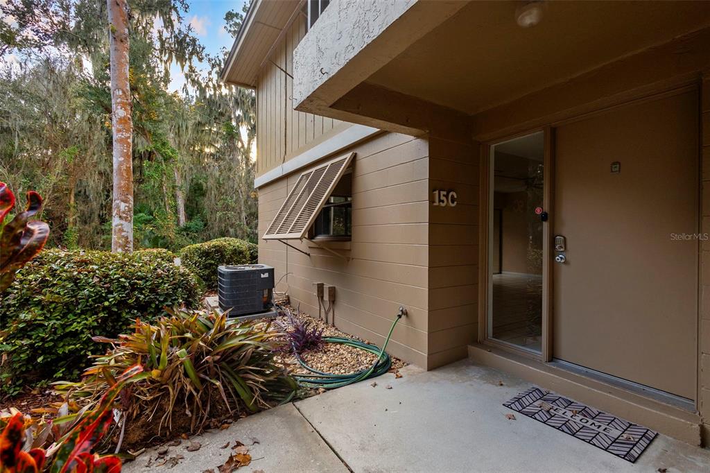 The exterior of a tan building features a front door, a window with shutters, and an AC unit — 120 HIBISCUS WOODS COURT UNIT 15C, DELTONA, FL
