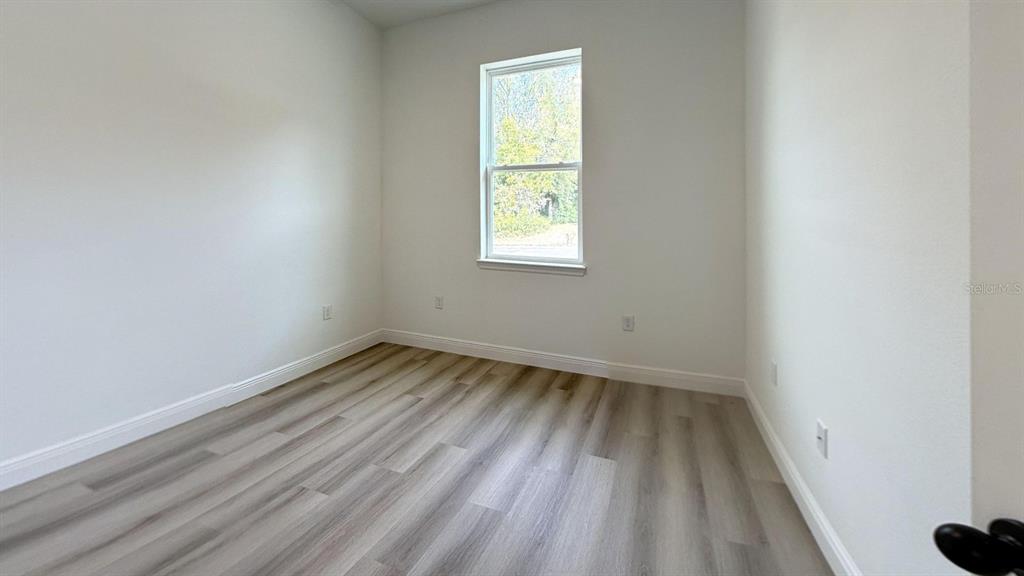 An empty room features light-colored wood-look flooring, white walls, and a single window — 8839 N CITRUS SPRINGS BOULEVARD, CITRUS SPRINGS, FL
