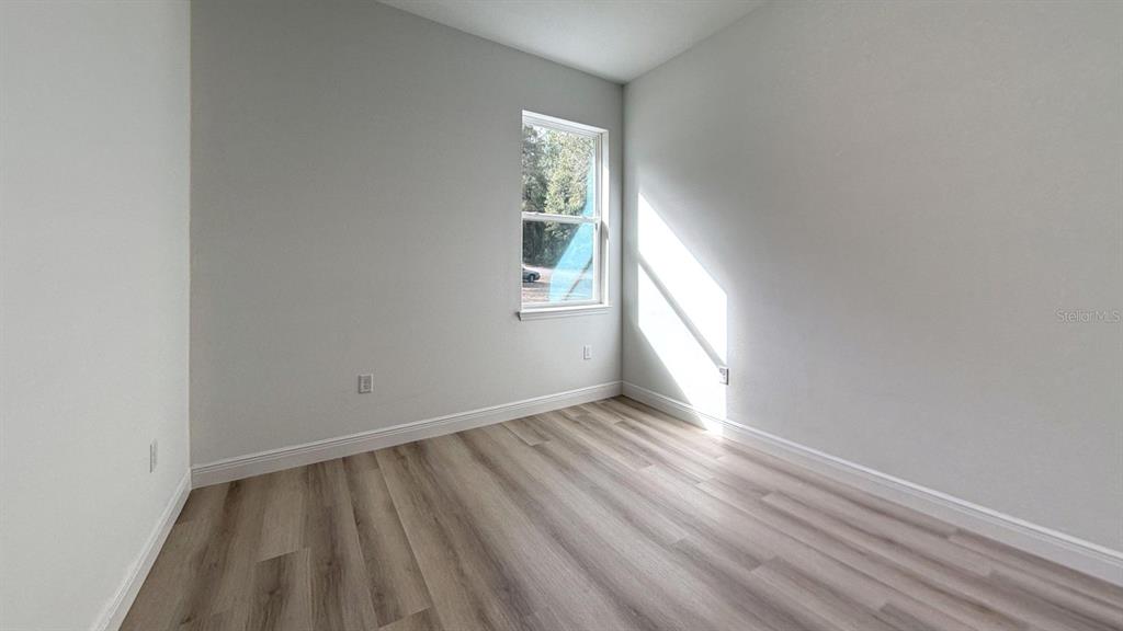 An empty room features light gray walls, wood-look flooring, and a single window — 8839 N CITRUS SPRINGS BOULEVARD, CITRUS SPRINGS, FL