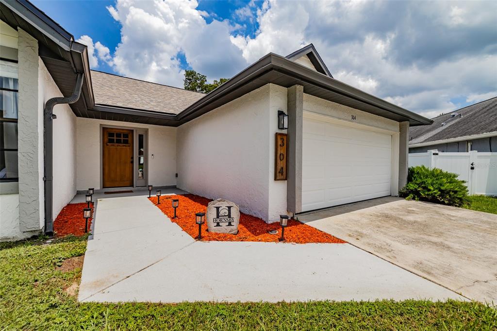 The exterior of a white house features a wooden front door and a garage — 304 SCARLET OAK COURT, SEFFNER, FL