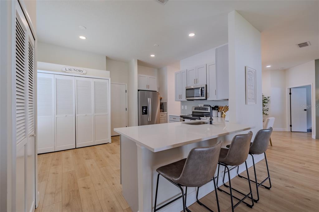 A modern kitchen features a white island with bar seating, stainless appliances, and laundry closet — 304 SCARLET OAK COURT, SEFFNER, FL