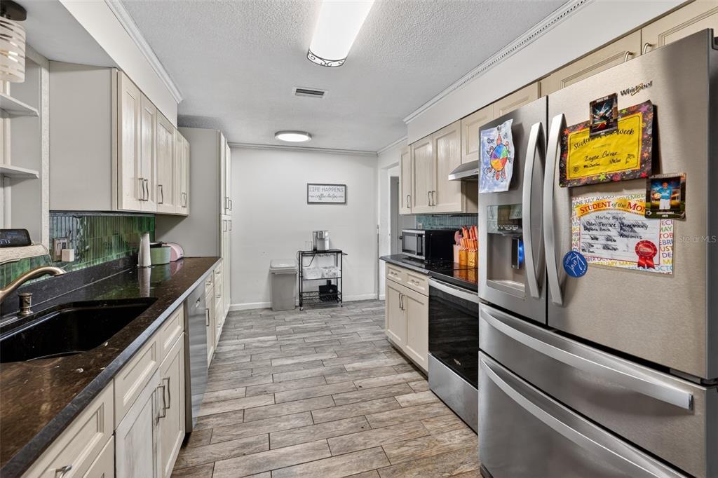 A kitchen features light-colored cabinets, dark countertops, stainless steel appliances, and wood-look tile flooring — 2354 GREEN STREET, SOUTH DAYTONA, FL