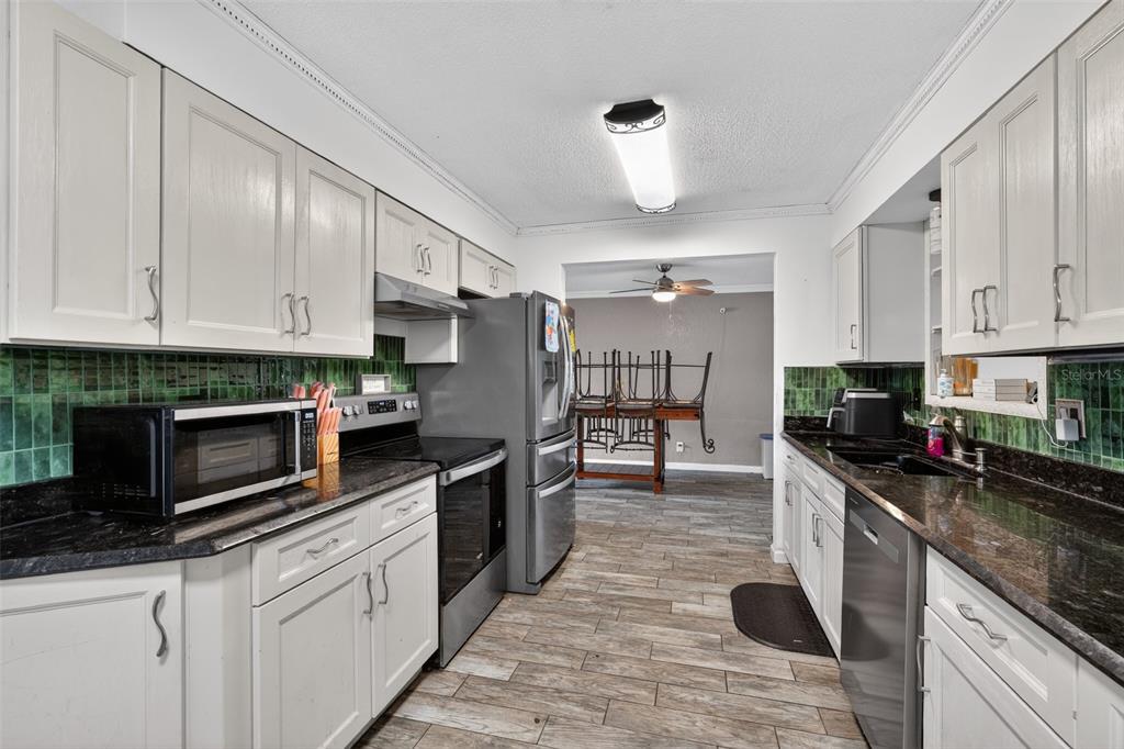 A kitchen with white cabinets, dark granite countertops, green tile backsplash, and stainless steel appliances — 2354 GREEN STREET, SOUTH DAYTONA, FL