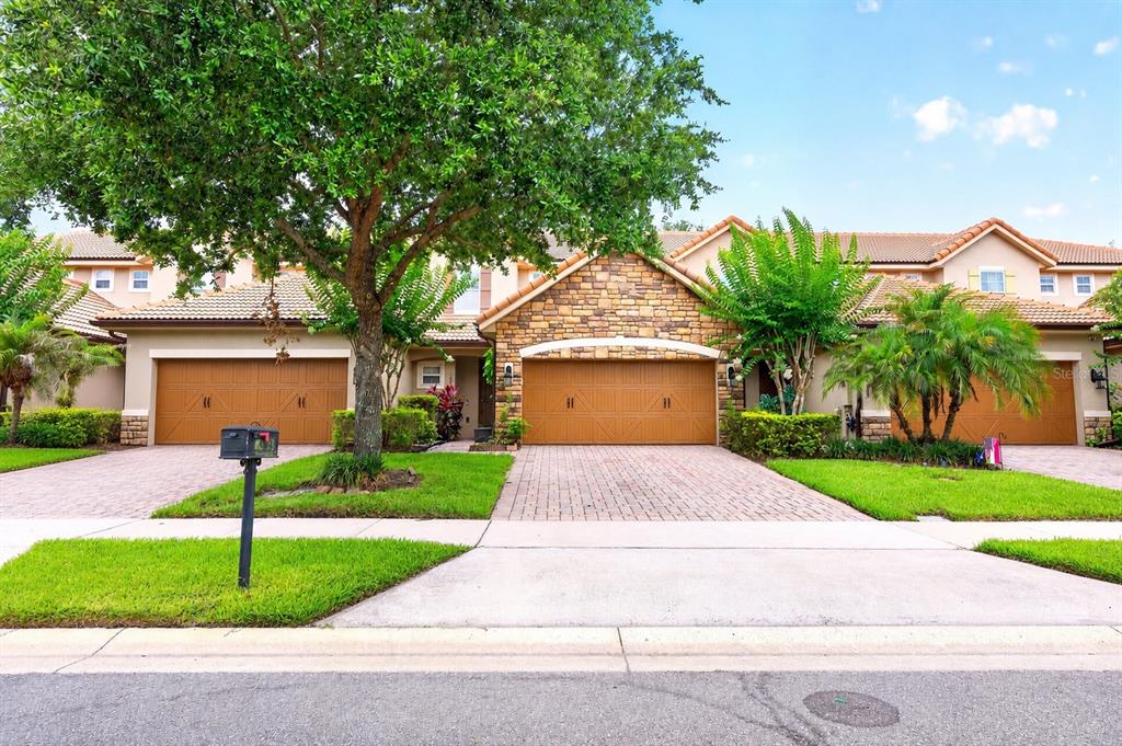 A row of townhomes with tan stucco, stone accents, tile roofs, and attached garages — 10329 BELFRY CIRCLE, ORLANDO, FL