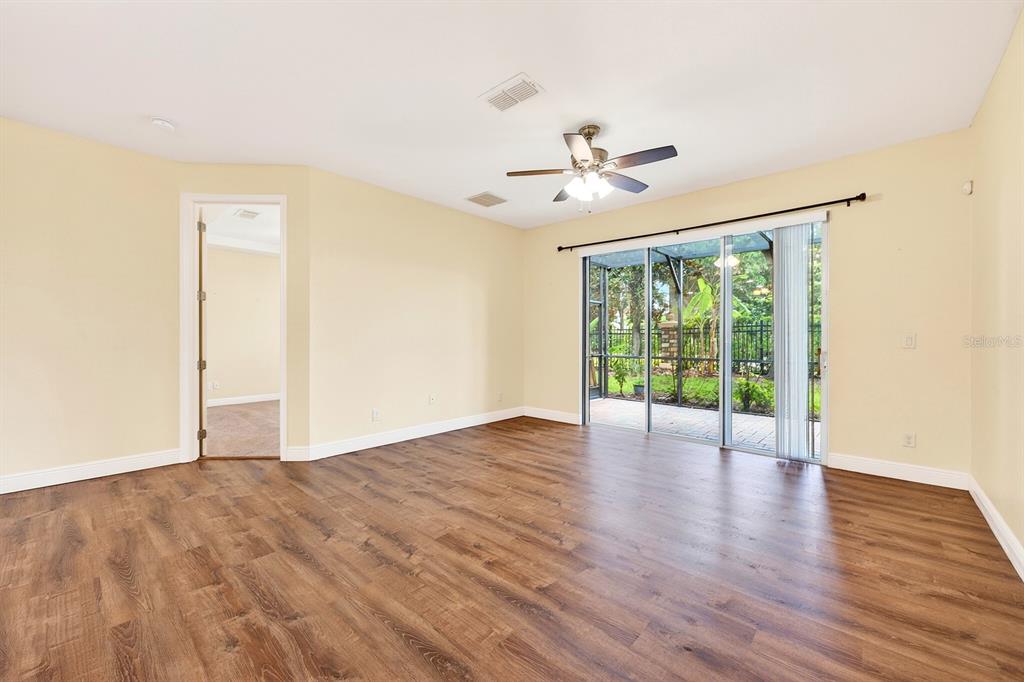 A spacious room with light yellow walls, wood-look flooring, a ceiling fan, and sliding glass doors — 10329 BELFRY CIRCLE, ORLANDO, FL
