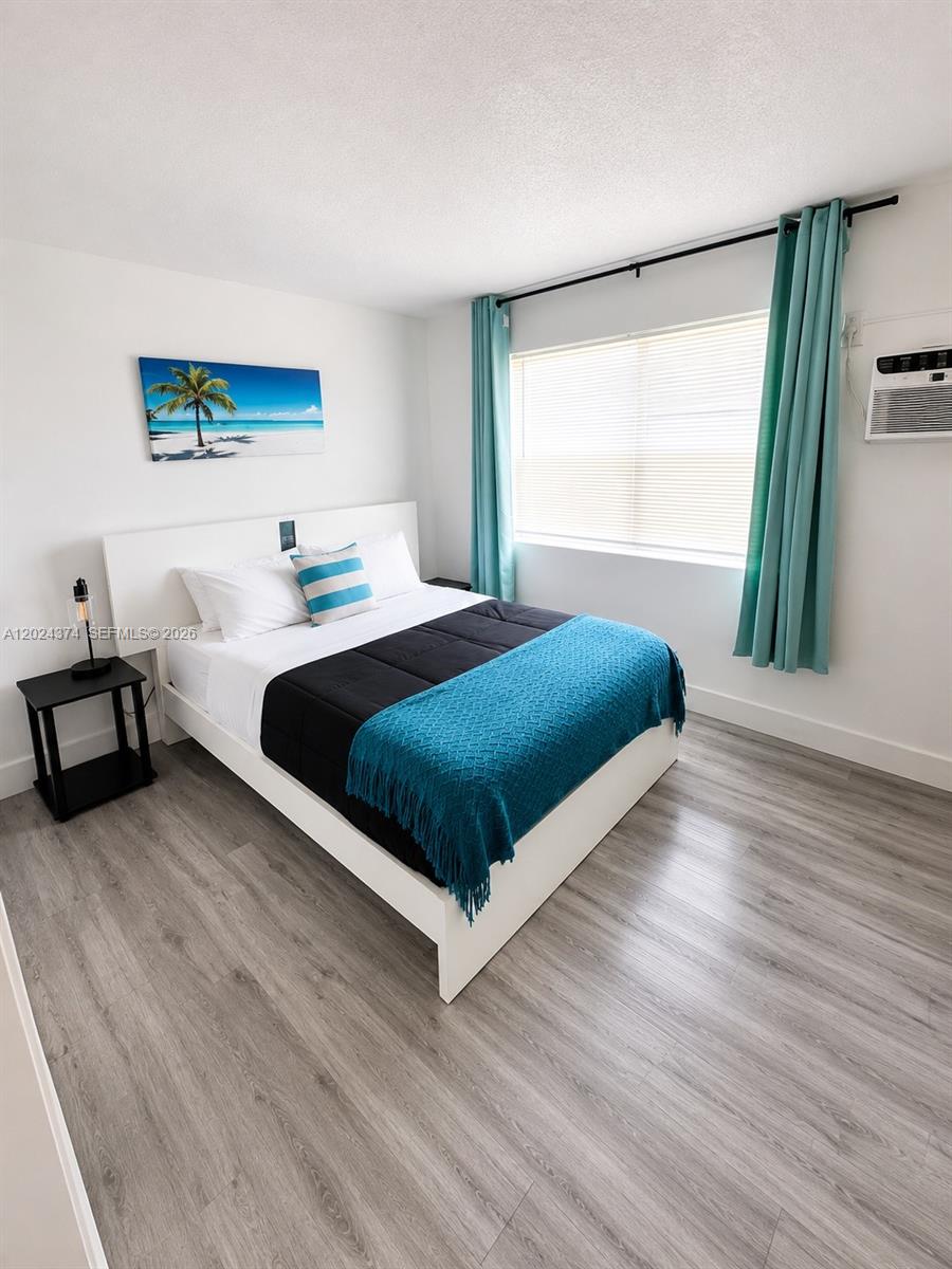 A bedroom features a bed with a blue throw, light wood flooring, and teal curtains — 3210 Canal Dr # 6, Pompano Beach FL 33062, POMPANO BEACH, FL