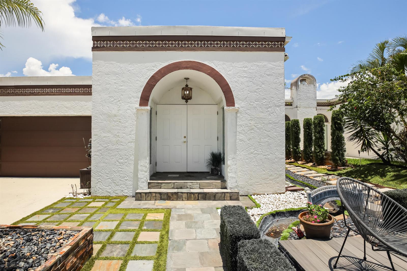The exterior of a white stucco house features an arched entryway and a stone walkway — LAKE WORTH, FL
